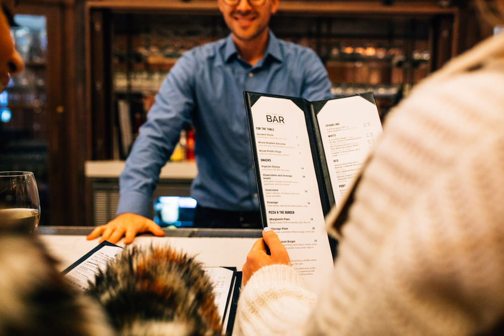 a couple looking at the bar menu while the bartender waits on them