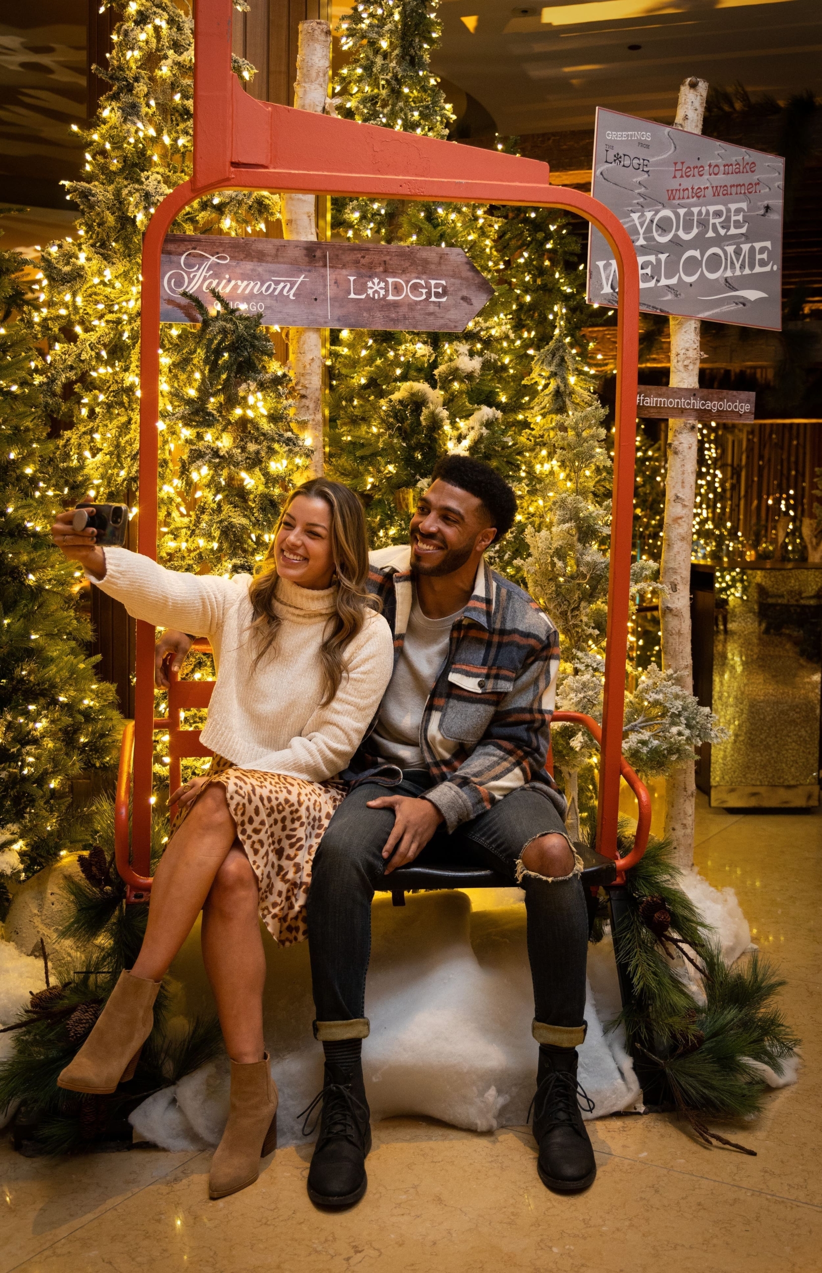 A couple sitting on a fake sea life in front of a few christmas trees